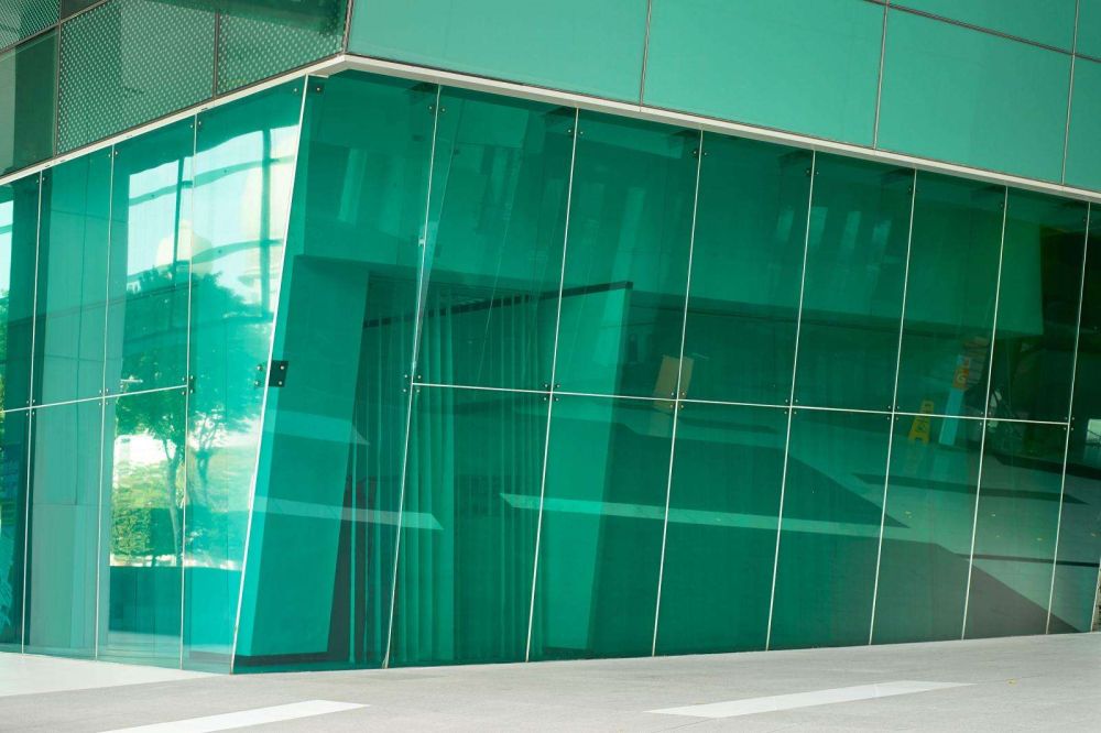 A modern building with an energy efficient green glass facade, featuring angular shapes and reflections.