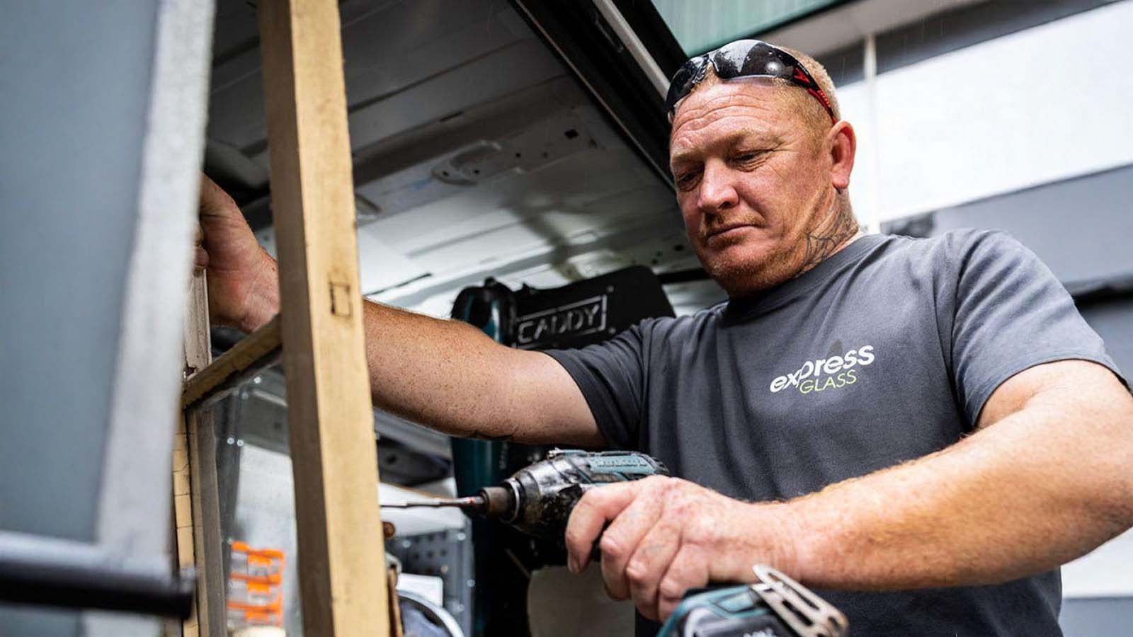 An Express Glass expert glazier using a power drill to work on a wooden frame inside a vehicle.
