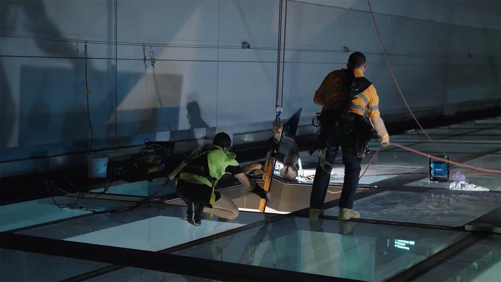 Two Express Glass specialist glaziers working on site at Westfields Bondi Junction, one kneeling and examining equipment while the other stands nearby, with large glass panels visible on the ground.