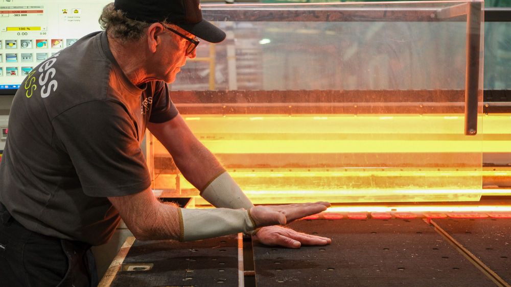 An Express Glass technician with glasses and a cap is working at a table, working on manufacturing engineered glass.