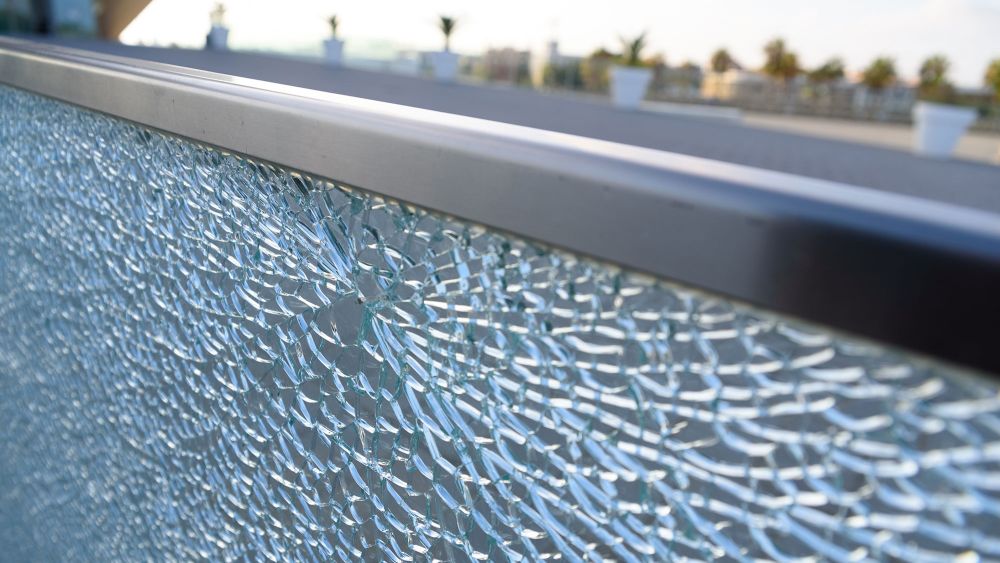 Close-up of a broken glass railing on a balcony, with a blurred outdoor background.