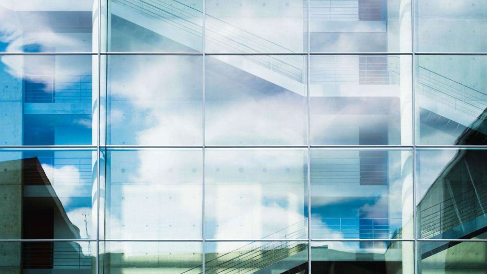 A modern glass building reflecting clouds and sky, showcasing a contemporary architectural style.