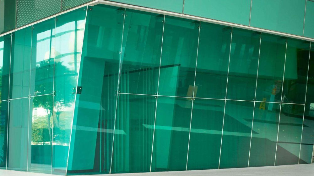 A modern building with an energy efficient green glass facade, featuring angular shapes and reflections.