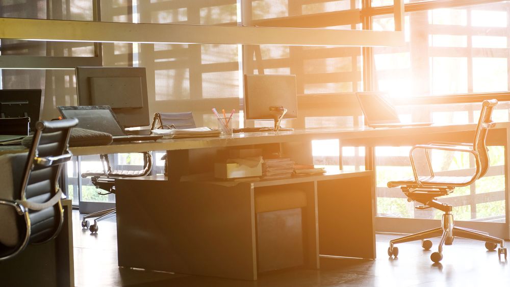 A modern office space featuring a large desk and several chairs, illuminated by natural light streaming through large energy efficient windows.