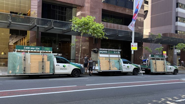 Three Express Glass service vehicles parked on a city street, each with large glass panels on the back, in front of a modern building.