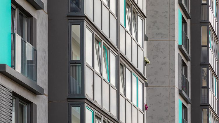 Close-up view of a modern strata managed apartment building with large windows and a mix of grey and turquoise materials.
