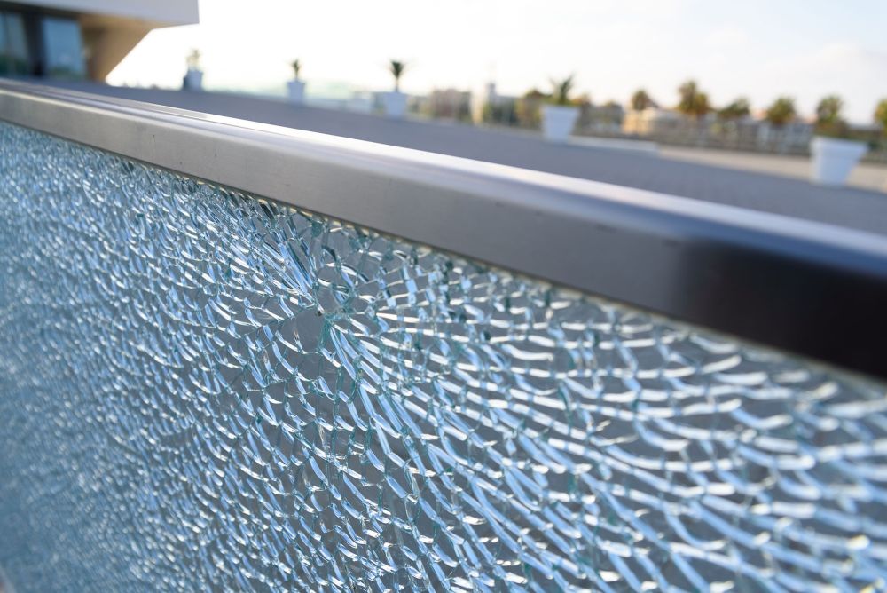 Close-up of a broken glass railing on a balcony, with a blurred outdoor background.