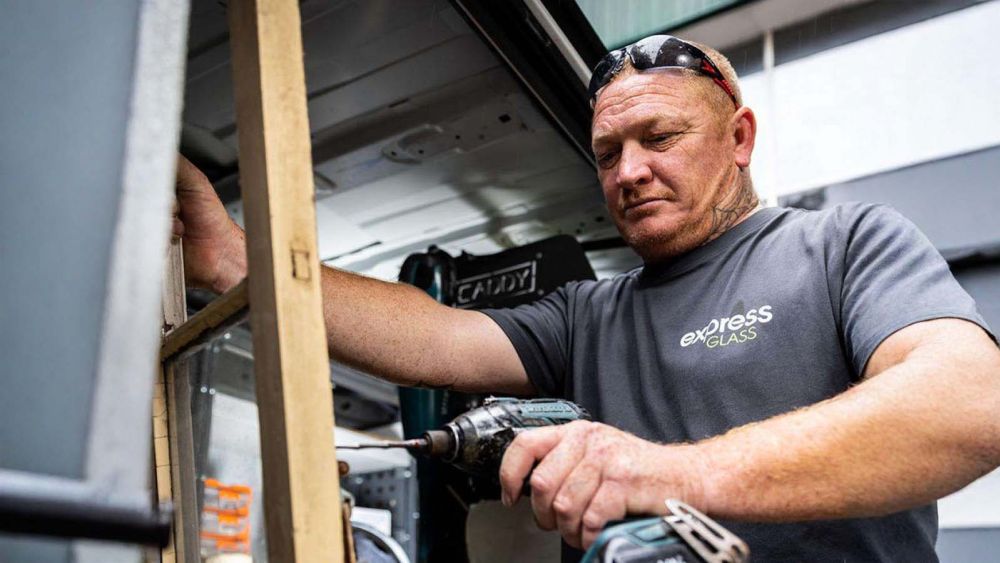 An Express Glass expert glazier using a power drill to work on a wooden frame inside a vehicle.
