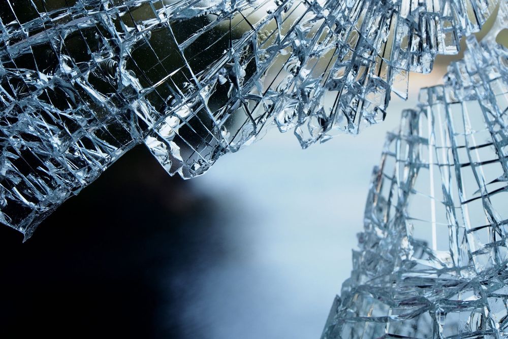 Close-up of broken glass with sharp edges, reflecting light, against a blurred dark background.