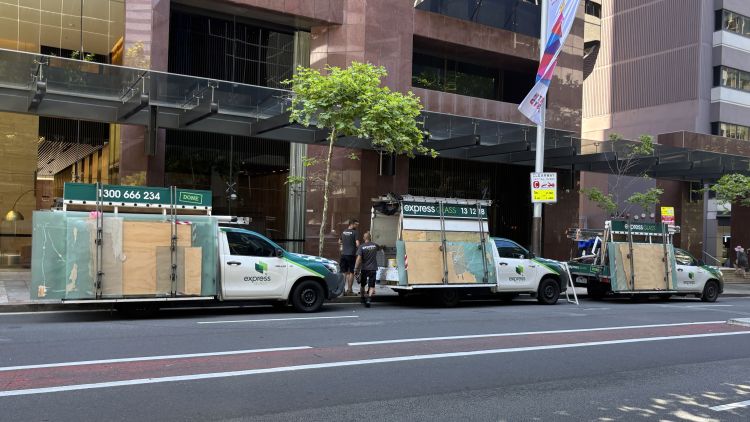 Three Express Glass service vehicles parked on a city street, each with large glass panels on the back, in front of a modern building.