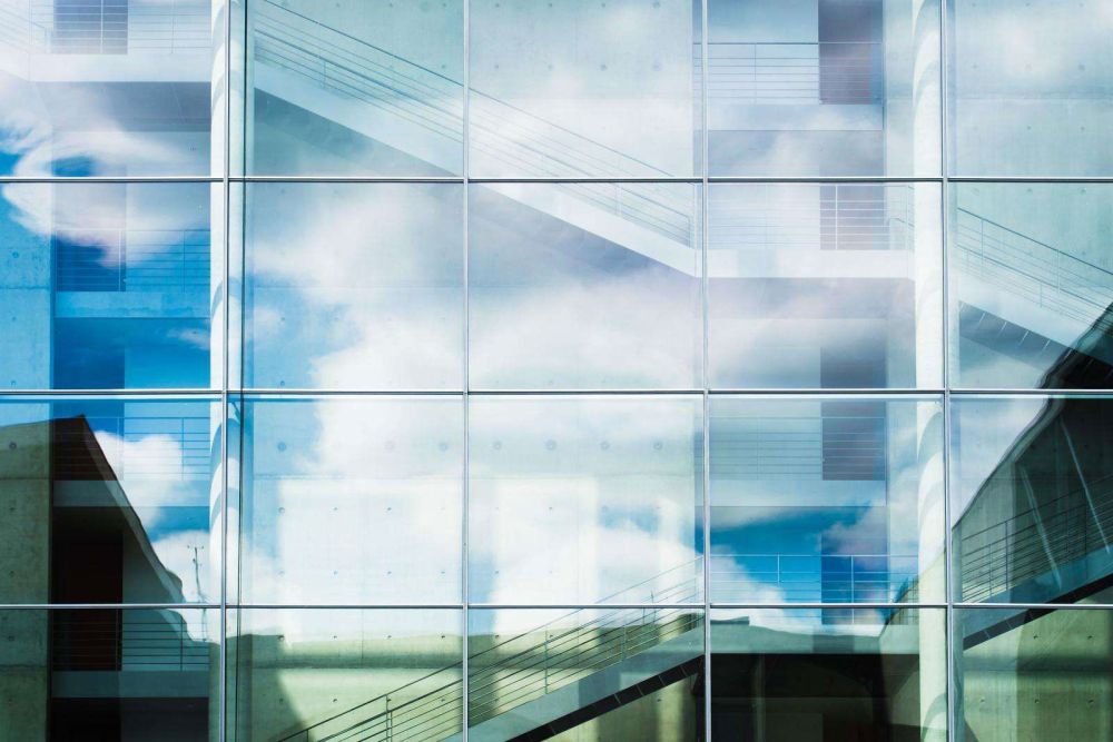 A modern glass building reflecting clouds and sky, showcasing a contemporary architectural style.